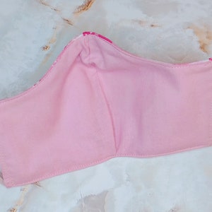 May include: Pink fabric face mask with white floral print. The mask has two ties for the ears.