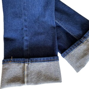May include: Close-up of dark blue denim jeans with folded cuffs. The cuffs are a lighter shade of blue and show the interior fabric. The jeans have visible stitching and a classic design.
