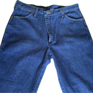 May include: A pair of dark blue denim jeans. The jeans have a classic five-pocket design, a button and zipper closure, and belt loops. The denim has a slightly faded appearance.