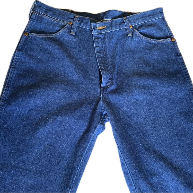 May include: A pair of dark blue denim jeans. The jeans have a classic five-pocket design, a button and zipper closure, and belt loops. The denim has a slightly faded appearance.