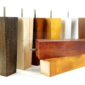 May include: Assortment of wooden furniture legs in various wood stains, including dark brown, light brown, reddish brown, and yellow. The legs are all square and have a threaded metal screw on top.