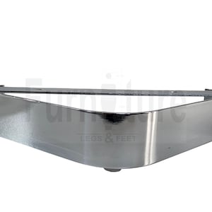 May include: A polished chrome furniture leg bracket. The bracket is triangular with rounded corners and a flat top. The words "LEGS & FEET" are printed in grey on the bottom right.