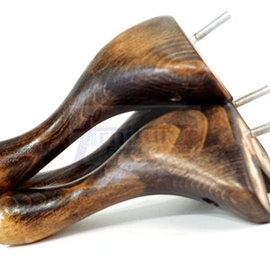 Może przedstawiać: Dwa ciemnobrązowe drewniane nóżki do mebli o zakrzywionym kształcie i kwadratowym wierzchołku. Każda nóżka ma wystający srebrny gwóźdź.