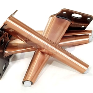 May include: Four copper-colored metal furniture legs with a tapered design and a flat mounting plate. Each leg has a white plastic foot pad.
