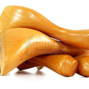 Puede incluir: Cuatro patas de muebles de madera sin terminar, apiladas unas sobre otras. Las patas son de color marrón claro y tienen un acabado liso y redondeado.