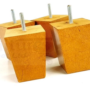 May include: Four wooden furniture legs with a light brown finish and silver metal screws. The legs are square shaped with a beveled edge.