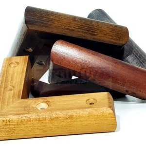May include: Four wooden corner brackets in different shades of brown, including natural, dark brown, and reddish brown. The brackets are all L-shaped and have rounded edges. They are designed to be used as furniture corner protectors.