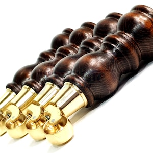 May include: Four dark brown wooden furniture legs with brass casters. The legs have a turned design and are attached to a screw.