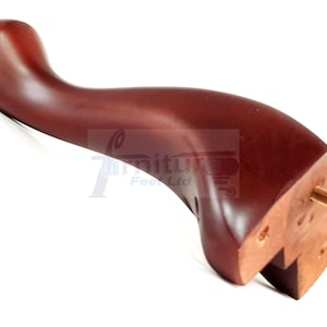 Puede incluir: Pata de mueble de madera marrón oscuro, curvada y con un tornillo de latón. La pata tiene un acabado liso y pulido. Componente de mueble para la construcción y reparación de muebles. Mide unos 20 cm de largo.