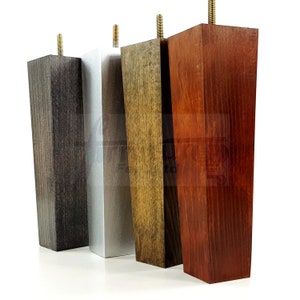 May include: Four wooden furniture legs in different finishes: dark brown, silver, brown, and red. The legs are tapered and have a square base.