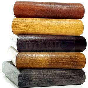 Op de afbeelding: Een stapel van vijf cilindrische houten meubelpoten met verschillende afwerkingen, waaronder roodbruin, licht eiken, donker espresso, medium walnoot en verweerd grijs. De tekst Furniture Feet Ltd is zichtbaar in het midden van de stapel.