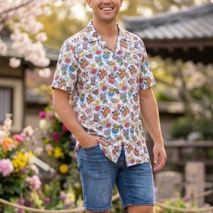 May include: A short-sleeved button-down shirt featuring a colorful all-over print of various Disney characters and icons, paired with blue denim shorts and white sneakers. The shirt has a classic collar and a straight hemline for a casual look.