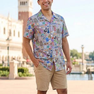 May include: A short-sleeved button-down shirt featuring a light gray background with a colorful all-over print of various landmarks, icons, and characters, paired with tan khaki shorts and white sneakers, creating a casual summer outfit.