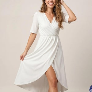 A woman in a white dress is smiling and posing with her hand on her head.