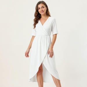 A woman wearing a white wrap dress with a high slit and a wrap neckline, smiling at the camera.