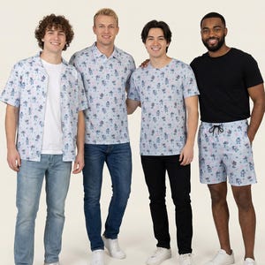 Puede incluir: Una colección de ropa azul claro con un patrón repetitivo de personajes de dibujos animados azules y flores rosas. El conjunto incluye una camisa de manga corta, un polo, una camiseta de cuello redondo y pantalones cortos con cordones negros.