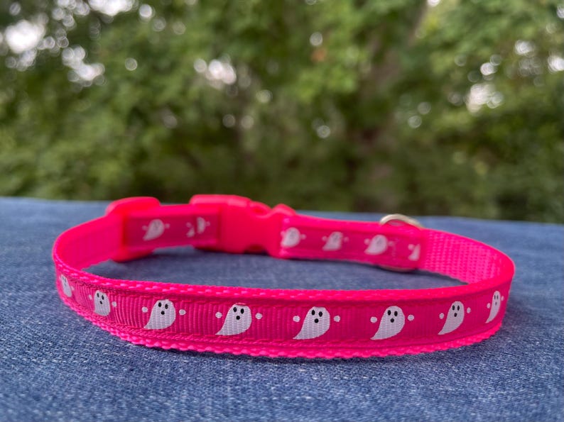 May include: A pink dog collar with a white ghost pattern. The collar is made of nylon and has a plastic buckle.