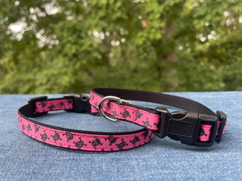 May include: Two pink dog collars with black skull and crossbones print. The collars have black adjustable buckles.