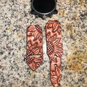 May include: Two brown leather watch straps with a sunflower design. The straps are for a smartwatch.