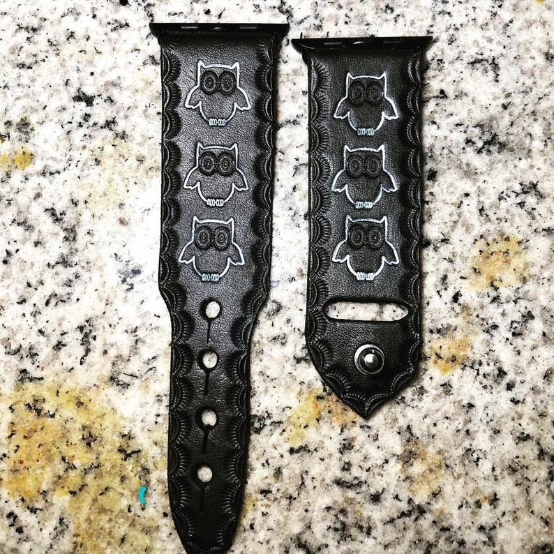 May include: Two black leather watch straps with white owl designs. The straps have a decorative scalloped edge and are designed for Apple Watches.