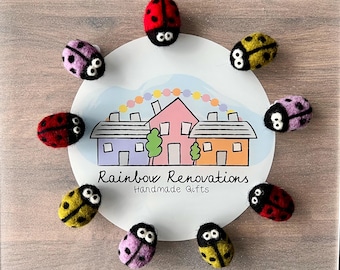 May include: Nine felt ladybug ornaments in various colors, including red, yellow, black, and pink. The ladybugs are arranged around a white circle with a house illustration and the text "Rainbow Renovations Handmade Gifts".