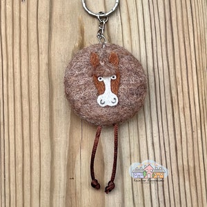 May include: Brown felt horse keychain with a white face and brown legs. The keychain is attached to a silver key ring.