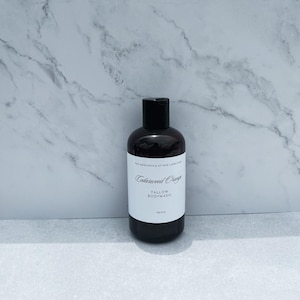 Könnte beinhalten: Eine dunkelbraune Kunststoffflasche mit Duschgel, einem schwarzen Verschluss und einem weißen Etikett. Das Etikett trägt den Text The Mercantile at Maz Lamb Farm, Cedarwood Orange, Tallow Bodywash und Net 8 oz in schwarzer Schrift auf weißem Grund.