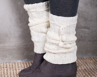 May include: A pair of gray suede wedge boots with white knitted leg warmers. The leg warmers have a fluffy pom-pom detail.