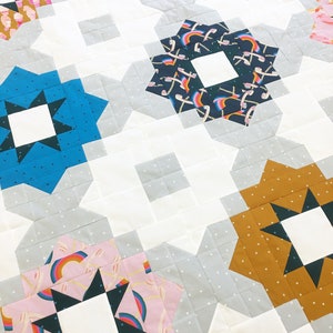 May include: A quilt with a white background and a variety of colorful fabric squares. The squares are arranged in a geometric pattern and feature different designs, including stars, rainbows, and geometric shapes.