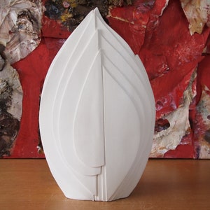 May include: White ceramic sculpture of a stylized flower with multiple layers. The sculpture is in the shape of a flame and has a smooth, matte finish.