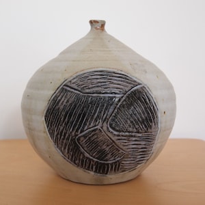 以下が含まれることがあります： 黒い幾何学模様が施された白い陶器の花瓶。花瓶は丸い胴体と細い首をしています。