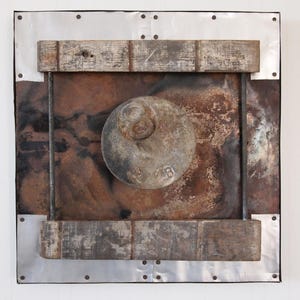 May include: A rusty metal square with a round, gray metal object in the center. The square is framed with wooden strips and a silver metal border.