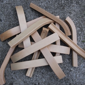 Op de afbeelding: Een stapel onafgewerkte, lichtbruine houten stoelonderdelen, waaronder gebogen en rechte stukken.