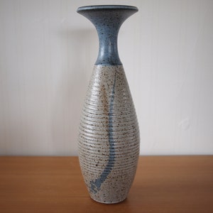 Könnte beinhalten: Eine Keramikvase mit einem hellblauen Oberteil und einem weißen Korpus mit braunen Flecken und einem blauen Streifen. Die Vase hat einen abgerundeten Boden und einen schmalen Hals.