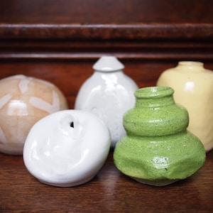 Peut inclure: Cinq vases en céramique de formes et de couleurs différentes. Les vases sont disposés sur une surface en bois. Les vases sont blancs, beiges, verts et jaunes.