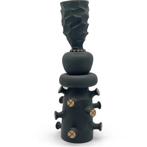 May include: A black ceramic sculpture with a textured top and a series of small, round, gold accents.