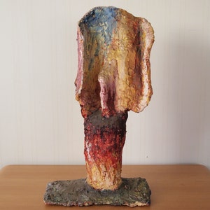 May include: Abstract ceramic sculpture with a textured surface. The sculpture is painted in shades of yellow, red, blue, and green.