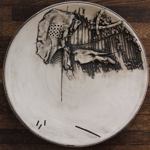 May include: A white ceramic plate with a black and white design. The design is abstract and features raised lines and textures.