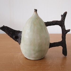 May include: A ceramic teapot with a light green glaze and a unique handle made from a dark brown branch.