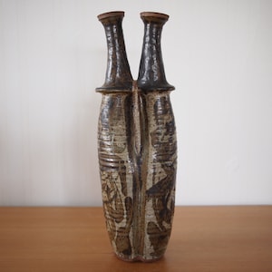 Könnte beinhalten: Eine braune und weiße Keramikvase mit zwei Ausgüssen. Die Vase hat eine strukturierte Oberfläche und ein einzigartiges Design.