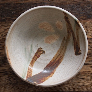 May include: A white ceramic bowl with brown and green brushstrokes. The bowl has a slightly rounded shape and a smooth, glazed finish.