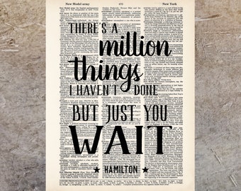 以下が含まれることがあります： 「There's a million things I haven't done but just you wait」というテキストと、下部に「Hamilton」という名前が書かれた、白黒のタイポグラフィーアートプリント。テキストは、ヴィンテージの辞書ページの背景に印刷されています。