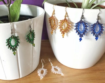 May include: Four pairs of beaded earrings in different colors, including green, gold, blue, and clear. The earrings are displayed on white ceramic pots with plants.