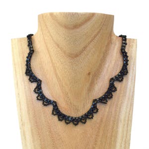 May include: A black beaded necklace with a scalloped design. The necklace is displayed on a wooden mannequin.