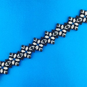 May include: A black and white beaded bracelet with a repeating flower design. The bracelet is made of small, round beads that are strung together to create a delicate and intricate pattern.