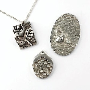 May include: Three silver pendants, one with a rose design, one with a bee design, and one with a geometric pattern.
