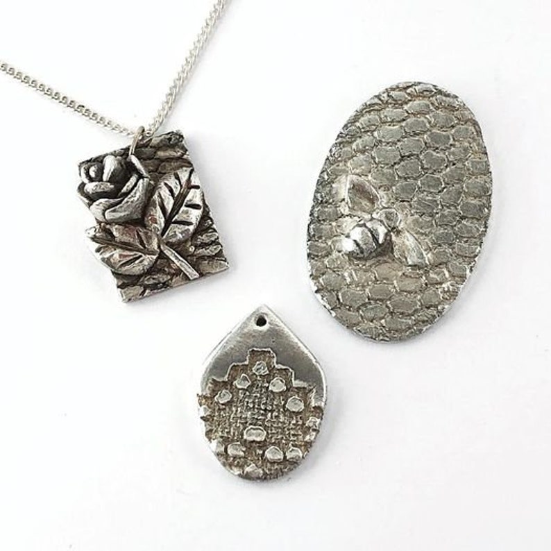 May include: Three silver pendants, one with a rose design, one with a bee design, and one with a geometric pattern.