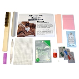 May include: Art Clay Silver Basic Kit with instructions, tools, and materials for making jewelry. The kit includes a silver clay bar, a polishing cloth, a sanding sponge, a brush, a tool, a small bottle of silver polish, and a small bottle of liquid. The kit also includes a small piece of silver jewelry.
