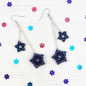 May include: A pair of dangle earrings with a silver chain and two dark blue star-shaped charms. The larger charm is a snowflake design and the smaller charm is a five-pointed star.