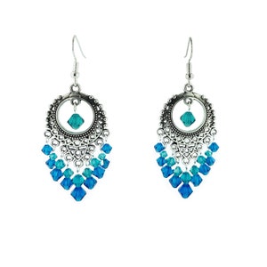 Puede incluir: Pendientes de plata con un diseño circular y un cristal azul en forma de lágrima en el centro. Los pendientes presentan múltiples capas de cristales azules más pequeños.
